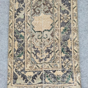 Könnte beinhalten: Rechteckiger Vintage-Teppich mit einem zentralen beigen Feld und aufwendigem Rand. Der Teppich weist ein abgenutztes Design mit dunkelblauen, grünen und beigen Mustern auf. Das Design umfasst florale und geometrische Motive.