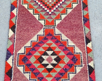 Puede incluir: Una alfombra rectangular con un diseño repetitivo de diamantes en rojo, naranja, negro, blanco y verde. La alfombra tiene un fondo burdeos y bordes con patrones geométricos. Ideal para un pasillo.
