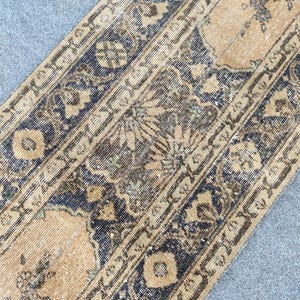 May include: A rectangular, distressed rug with a beige central field and dark blue borders. The rug features intricate floral and geometric patterns in shades of brown, beige, and blue, creating a vintage aesthetic.