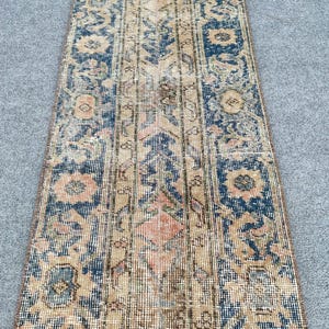 May include: A rectangular, vintage-style rug with a distressed appearance. The rug features a central beige field with intricate floral and geometric patterns in navy blue, peach, and brown. The rug's design is symmetrical, with a border of navy blue.