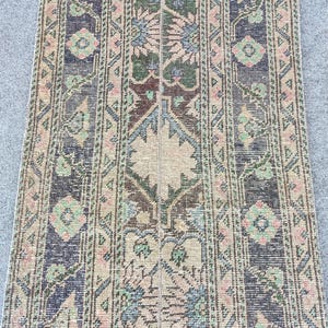 May include: A rectangular woven rug featuring a vertical striped pattern with intricate geometric and floral motifs. The colour palette includes muted shades of dark charcoal, dusty pink, sage green, and beige, arranged in repeating symmetrical bands.