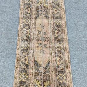 May include: A rectangular, vintage-style rug with a distressed appearance. The rug features a central panel in a light peach colour, bordered by darker brown and black patterns. Yellow floral motifs are interspersed throughout the design, creating a warm aesthetic.