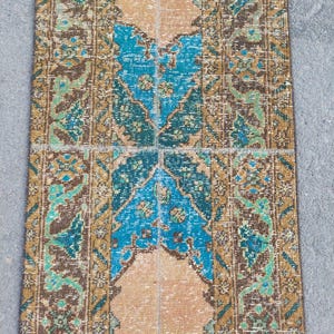 Pode incluir: Um tapete retangular com uma aparência vintage e desgastada. O tapete apresenta um design central em tons de azul e bege, emoldurado por bordas em marrom, verde e dourado. O design do tapete tem um intrincado padrão floral.
