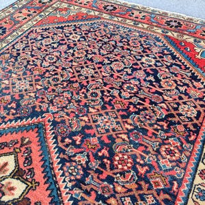 Peut inclure: Un tapis rectangulaire pr&eacute;sentant un champ central bleu fonc&eacute; avec un motif dense et r&eacute;p&eacute;titif de formes g&eacute;om&eacute;triques et florales dans des tons corail, cr&egrave;me et bleu clair. Le tapis est bord&eacute; d'une large bordure corail &agrave; motifs floraux.