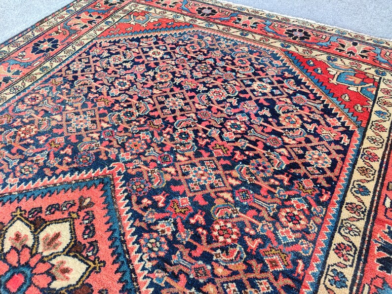 Peut inclure: Un tapis rectangulaire pr&eacute;sentant un champ central bleu fonc&eacute; avec un motif dense et r&eacute;p&eacute;titif de formes g&eacute;om&eacute;triques et florales dans des tons corail, cr&egrave;me et bleu clair. Le tapis est bord&eacute; d'une large bordure corail &agrave; motifs floraux.