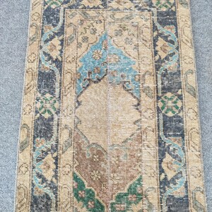 Peut inclure: Un tapis rectangulaire de type chemin de couloir avec un motif central en médaillon dans des tons de beige, marron et vert. La bordure est bleu foncé avec des motifs floraux complexes en bleu clair et vert. La texture semble tissée et usée.