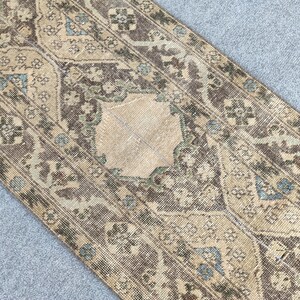 Könnte beinhalten: Ein Teppich im antiken Stil mit einem abgenutzten Aussehen. Er hat ein beiges Mittelmedaillon, das von aufwendigen floralen und geometrischen Mustern in Braun-, Beige- und Türkistönen umgeben ist. Das Design deutet auf einen Vintage- oder Orientstil hin.