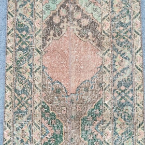 May include: A rectangular, distressed vintage rug with a central medallion design. The rug features a colour palette of muted pink, brown, green, and blue. The intricate patterns include floral and geometric motifs, creating a classic, aged aesthetic.