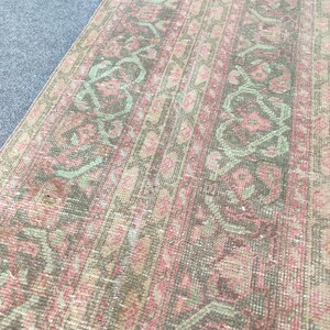 Könnte beinhalten: Ein rechteckiger Vintage-Teppich mit verblasstem, abgenutztem Aussehen. Der Teppich hat ein sich wiederholendes Muster aus floralen und geometrischen Designs in Rosa, Grün und Braun. Die Kanten sind leicht abgenutzt, was seinen antiken Charme unterstreicht.