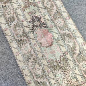 Könnte beinhalten: Ein rechteckiger Teppich im Vintage-Stil mit verblasstem, abgenutztem Aussehen. Der Teppich hat einen beigefarbenen Hintergrund mit einem sich wiederholenden Muster aus floralen und geometrischen Designs in Braun-, Rosa- und Grüntönen. Ideal für Wärme und Charakter.