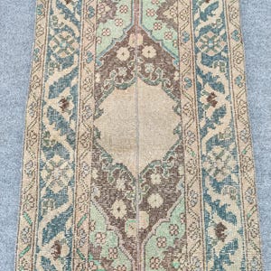 May include: A rectangular, vintage rug with a central brown and green floral design. The rug has a beige background with blue and beige borders. The design features intricate floral and geometric elements, creating a classic, aged appearance.