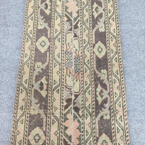 Può includere: Un tappeto rettangolare in stile vintage con un motivo dettagliato. Il tappeto presenta un design centrale nei toni del marrone, beige e verde, con motivi geometrici e floreali. I bordi sono bordati con un motivo simile.
