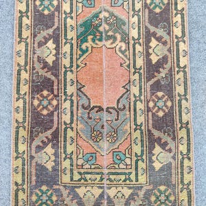 Könnte beinhalten: Ein rechteckiger Vintage-Teppich mit einem zentralen Design in Pfirsich-, Türkis- und Grüntönen. Der Teppich hat einen dunkelbraunen Rand mit floralen und geometrischen Mustern. Das Design ist symmetrisch und detailliert.
