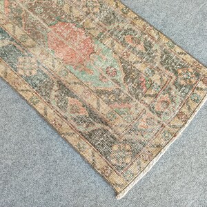 May include: A rectangular rug with a distressed appearance, showcasing a central medallion design. The rug's colour scheme includes beige, brown, green, and coral accents. The edges of the rug are slightly frayed, enhancing its vintage style.