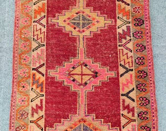 Puede incluir: Una alfombra rectangular vintage con un campo central rojo oscuro. La alfombra presenta patrones geométricos en tonos de rosa, beige, naranja y azul. Los bordes tienen diseños intrincados, lo que se suma a la estética tradicional de la alfombra.