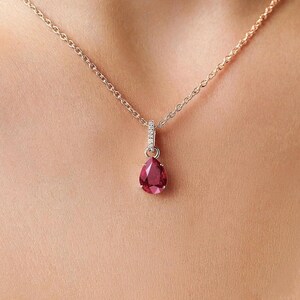 Può includere: Una collana delicata con un ciondolo a forma di goccia di colore rosso intenso, sospeso a una sottile catenina di metallo. L'occhiello del ciondolo è impreziosito da piccole pietre chiare e scintillanti che aggiungono luce alla pietra centrale.