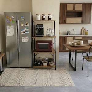 May include: A kitchen scene featuring a stainless steel refrigerator with magnets, a wooden shelf unit with a coffee maker and microwave, and a patterned rug. The kitchen has wooden cabinets and a dining table.