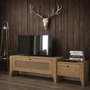 Puede incluir: Un mueble de TV de madera marrón claro con un panel frontal tejido y una mesa auxiliar a juego. Un televisor de pantalla plana negro se encuentra encima. Un cráneo de ciervo y astas están montados en la pared de paneles de madera marrón oscuro.