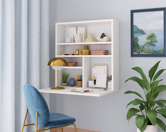 May include: A white wall-mounted desk with a built-in shelf unit, featuring various decorative items and office supplies. A blue chair with gold legs sits in front of the desk. A gold lamp and a framed picture are also visible.