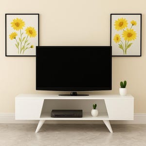 Könnte beinhalten: Ein moderner weißer TV-Schrank mit einem schwarzen Flachbildfernseher, flankiert von zwei gerahmten Sonnenblumen-Kunstdrucken. Ein schwarzer DVD-Player und kleine Topfpflanzen sorgen für dekorative Akzente. Der Schrank hat abgewinkelte Beine und ein minimalistisches Design.