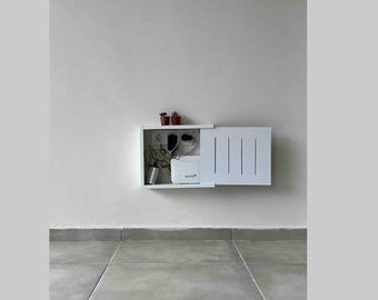 Può includere: Un armadio bianco a muro con una porta che si apre per rivelare un router e altri cavi. Ci sono due piccole piante in vaso sopra l'armadio.