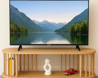 May include: A modern entertainment center with a large flat-screen TV displaying a scenic lake view. The light wood cabinet features a rounded design with vertical slats, holding books, a white sculpture, and a red toy car. The TV is approximately 55 inches.