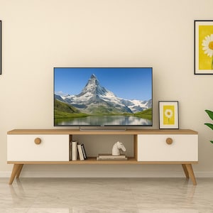 May include: A modern living room setup with a large TV showing a mountain scene. A wooden and white cabinet is below the TV, with daisy art on the walls. A potted plant and a small side table with flowers add to the room's decor.