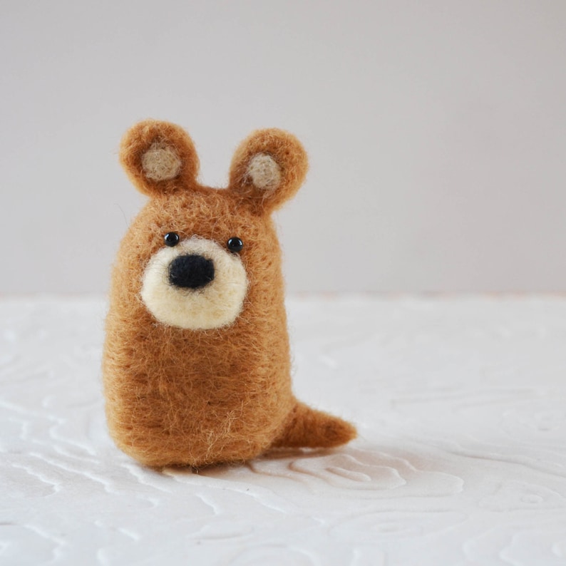 Pode incluir: Figura de animal de feltro feita &agrave; m&atilde;o em forma de urso. O urso &eacute; castanho com um focinho creme e olhos pretos pequenos. Tem orelhas pequenas e arredondadas e uma cauda min&uacute;scula. A figura est&aacute; em p&eacute;.