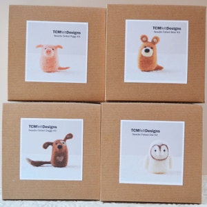 Pode incluir: Quatro caixas de cart&atilde;o castanhas com etiquetas brancas com kits de animais de feltro com agulha. Os kits incluem um porco, um urso, um c&atilde;o e uma coruja. Cada etiqueta exibe o texto "TCMfeltDesigns Needle Felted" seguido do nome do animal.