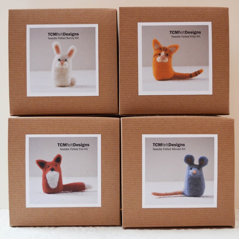 Pode incluir: Quatro caixas de cart&atilde;o castanhas, cada uma com uma etiqueta branca com um kit de animais de feltro com agulha. Os kits incluem um coelho, um gato, uma raposa e um rato. Os r&oacute;tulos dizem "TCMfeltDesigns Needle Felted [Animal] Kit."