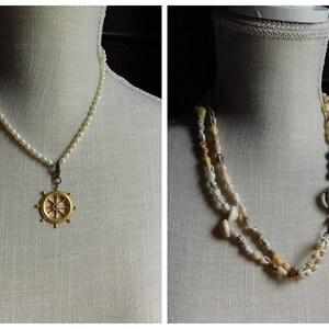 May include: Two necklaces on display mannequins. The first necklace is a white pearl strand with a gold ship's wheel pendant. The second necklace is a multi-strand of small white seashells with a gold ring and clasp.