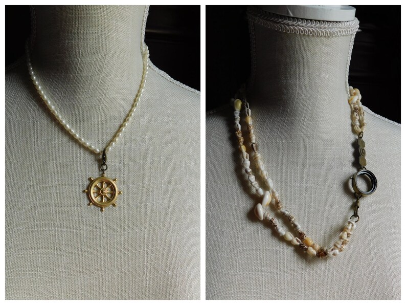 May include: Two necklaces on display mannequins. The first necklace is a white pearl strand with a gold ship's wheel pendant. The second necklace is a multi-strand of small white seashells with a gold ring and clasp.