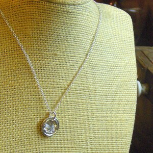 May include: A silver chain necklace with a round silver pendant. The pendant has a textured design.