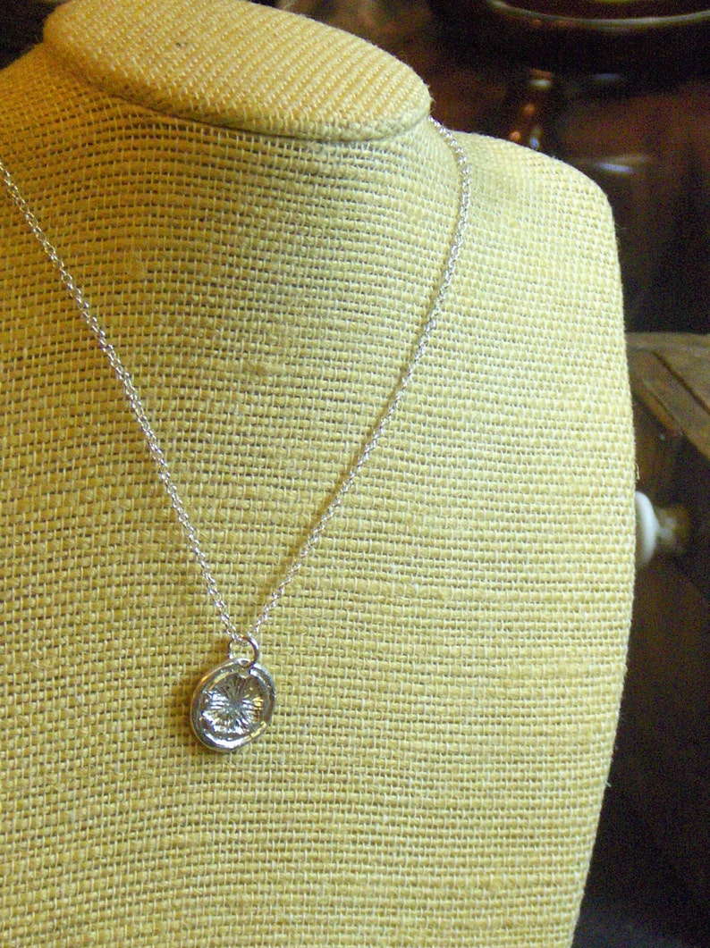 May include: A silver chain necklace with a round silver pendant. The pendant has a textured design.