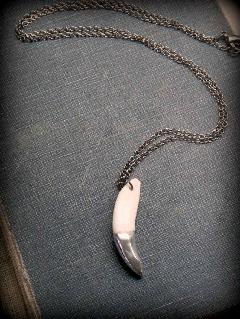 May include: A silver chain necklace with a white ceramic tooth pendant. The tooth is partially silvered, giving it a two-tone effect.