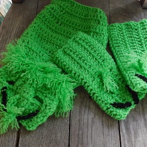 May include: A set of green crocheted leg warmers with black trim. The leg warmers are made with a fuzzy yarn and have a textured design.