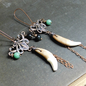 May include: A pair of earrings with a filigree design, green and black beads, and a tooth-shaped pendant. The earrings are made of copper and have a vintage look.
