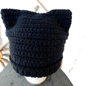 May include: Black crocheted beanie with cat ears. The beanie is made of a soft, fuzzy yarn and has a simple, classic design.