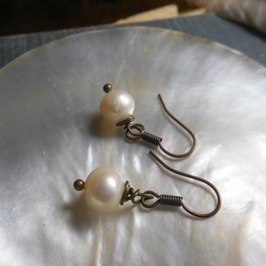 May include: A pair of pearl earrings with bronze-colored hooks. The pearls are white and round.