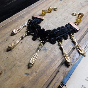May include: A black lace choker necklace with gold-toned metal accents and dangling charms. The necklace has a delicate and intricate design.