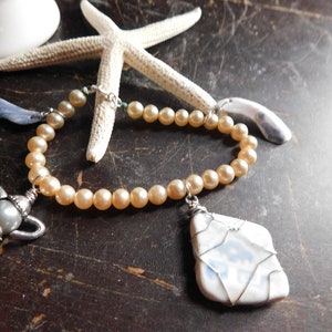 May include: A pearl bracelet with a teapot charm, a blue and white ceramic charm, and a shell charm. The bracelet is on a brown wooden surface.