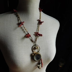 May include: A necklace with a gold chain and red coral accents. The pendant is a round, antique-looking locket with a glass window.