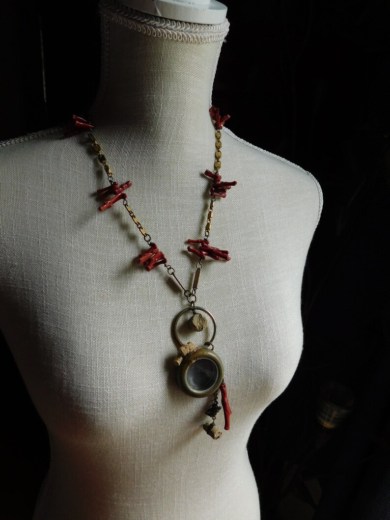 May include: A necklace with a gold chain and red coral accents. The pendant is a round, antique-looking locket with a glass window.