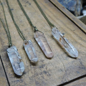Puede incluir: Cuatro colgantes de cristal de cuarzo transparente en cadenas de bronce. Los cristales son de diferentes tamaños y formas, y tienen un aspecto natural y en bruto.