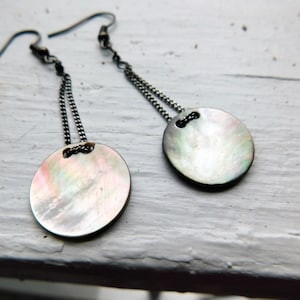 May include: A pair of silver earrings with a round, iridescent shell pendant on each earring. The earrings are suspended from a silver chain.