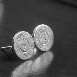May include: A pair of silver earrings with a circular design. The earrings feature the words "Winchester" and "Western" on them.