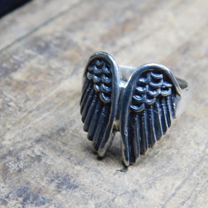 May include: A silver ring featuring a detailed design of angel wings.