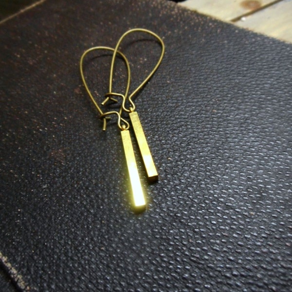 Könnte beinhalten: Ein Paar goldfarbene Ohrringe mit einem einfachen Balken-Design. Die Ohrringe sind aus dünnem Metall gefertigt und haben einen zarten, minimalistischen Stil.