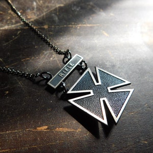 May include: A black metal military pendant with a cross design and a silver bar that reads "RIFLE".