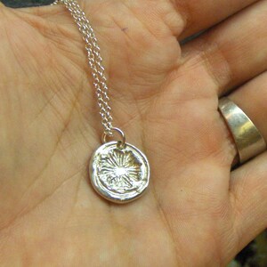 May include: A silver necklace with a round pendant featuring a detailed floral design. The pendant is slightly raised and has a textured surface.